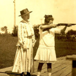 Annie Oakley watches as young girl takes aim